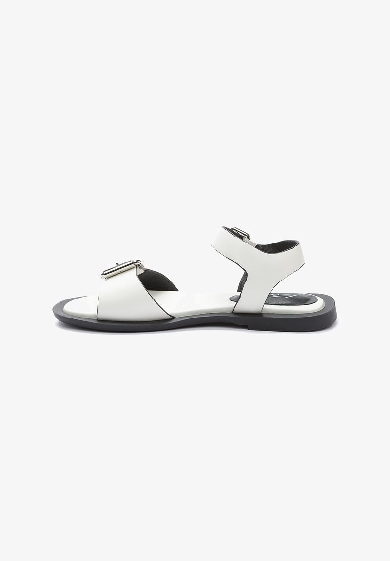 Sandalias de cuero blanco con un diseño de tiras cruzadas, correa para el tobillo ajustable y una suela de goma negra. Detalle de hebilla en la parte delantera.
