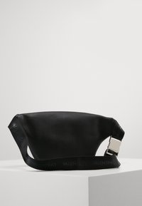 Μαύρη δερμάτινη τσάντα χιαστί με λεία υφή, κομψό κυρτό σχήμα και λωρίδα με λογότυπο και μεταλλική πόρπη.