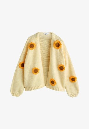 Cremefarvet strikket cardigan med store gule og brune hæklede solsikkeapplikationer på front og ærmer, med et løst, åbent frontdesign.