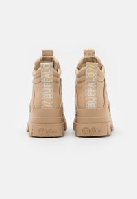 Baskets montantes tan avec semelles renforcées, tige en cuir texturé et languettes imprimées de logo blanches. Design épais et respirant avec des accents de coutures.