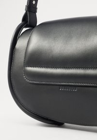 Borsa a tracolla in pelle nera con forma arrotondata, texture liscia, cuciture visibili e nome del marchio impresso. Inclusa tracolla regolabile.