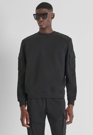 Zwart sweatshirt met een ronde hals, schouderaccenten en twee zijzakken. Gemaakt van zachte stof en heeft een ontspannen pasvorm.
