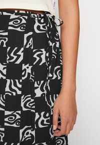 Saia em preto e branco com padrões que apresentam designs abstratos, cintura atada e uma textura de tecido suave. Acentos de costura visíveis.