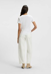 White short-sleeve t-shirt, fitted at the waist, gray wide-leg jeans, light fabric, and beige heeled ankle boots, viewed from the back.