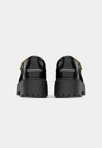 Sapatos pretos de pele polida com sola plataforma espessa, apresentando um accent de fivela dourada e detalhes de costura branca contrastantes.