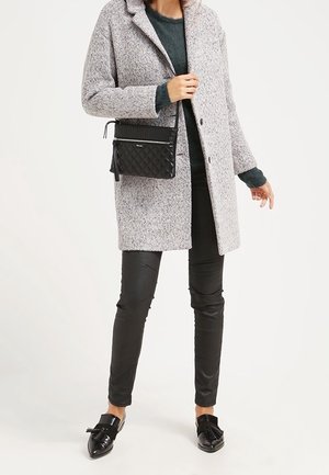 Osoba ubrana w szary wełniany płaszcz, ciemnozielony sweter, czarne skórzane spodnie, czarne mokasyny z frędzlami oraz niosąca małą czarną pikowaną torebkę na pasku przez ramię.