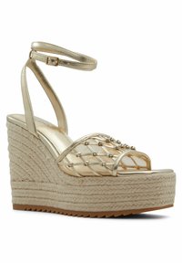 Zlaté klínové sandály s tkanou juty platformou, průhledným horním pásem s kovovými akcenty, nastavitelným kotníkovým páskem a texturovanou podrážkou.