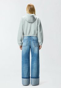 Felpa grigia corta con cappuccio e orlo elastico abbinata a jeans blu sbiaditi a gamba larga con risvolti e tasche posteriori.