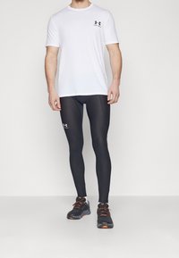 Camiseta blanca de manga corta con logo negro, combinada con leggins negros y zapatillas deportivas negras con acentos naranjas. Diseño simple y ajustado.
