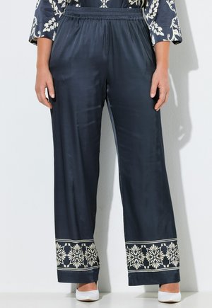 Pantaloni larghi navy con vita elastica e motivo a bordura floreale bianca agli orli, indossati con scarpe bianche a punta e top decorato.