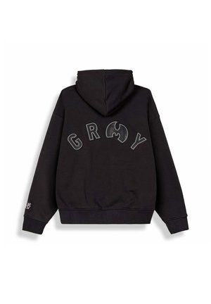 Sudadera negra con capucha con grandes letras bordadas "G R O Y" y un símbolo estilizado en la espalda, y un pequeño parche en el puño de la manga izquierda.