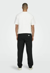 Weißes kurzärmliges T-Shirt kombiniert mit schwarzen Hosen. Die Hosen verfügen über eine Gesäßtasche und ein Etikett nahe dem Bund. Einfaches und funktionales Design.
