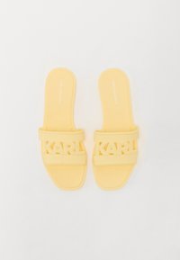 Gula gummisandaler med dubbla remmar som har utskurna "KARL"-logotyper. Platt sula med minimalistisk design och slät textur.