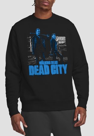 Man wearing black sweatshirt with blue graphic of two characters holding weapons in front of buildings and text "Walking Dead Dead City."