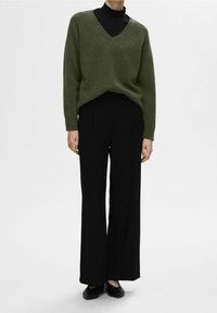Maglione verde oliva a scollo a V con vestibilità larga, abbinato a pantaloni neri a gamba larga. Tessuto a maglia morbida, design casual. Ballerine nere completano il look.