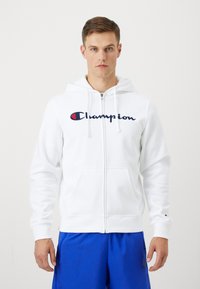 Hvit zip-up hettegenser med frontlomme, brodert "Champion"-logo i marineblått og rødt på brystet, og justerbar snorhette.