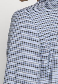 Rutig kavaj med ett ljusblått och svart mönster, strukturerad design och texturerad tyg. Visar en klassisk skräddarsydd passform.