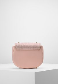 Różowa skórzana torba na ramię o zaokrąglonym kształcie i teksturowanej górnej klapie przypominającej skórę pytona. Złote akcenty metalowe podkreślają projekt.