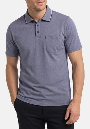 Homme portant un polo bleu chiné à manches courtes avec col et poche poitrine, associé à un pantalon noir, debout les mains dans les poches.