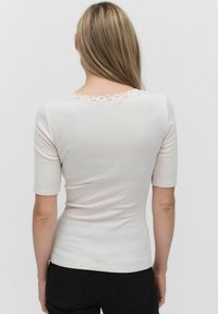 Hvid ribbet top med korte ærmer og en scallop-blondekant detalje på ryggen. Tæt design med en glat tekstur.