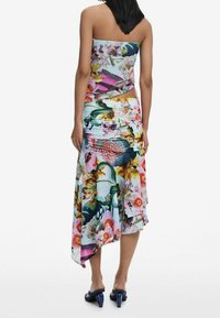 Un haut sans bretelles à imprimé floral coloré et une jupe asymétrique en tissu léger. Les motifs notables incluent des poissons et des fleurs. Sandales bleu foncé.