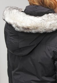 Black jacket with a fur-lined hood, featuring a textured gray and white fur trim and a smooth, matte finish on the fabric.