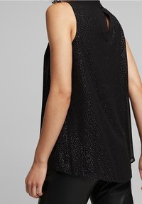 Sort ærmeløs top med løs pasform, der har en nøglehulslukning bagpå og spredte metalliske accenter for ekstra tekstur og visuel interesse.