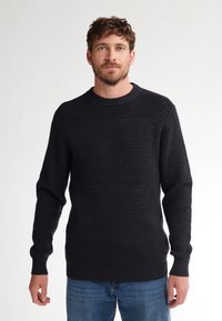 Donkerblauwe gebreide trui met een ronde hals en geribbelde manchetten, gecombineerd met blauwe jeans. Eenvoudig ontwerp zonder zichtbare patronen.