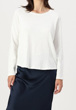 Top bianco a maniche lunghe con scollatura rotonda e maniche raglan, abbinato a una gonna in satin blu scuro. Tessuto strutturato, vestibilità comoda.