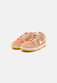 Barna és korall Nike tornacipők velúr felsőrésszel, perforált orral, fehér swoosh logóval és sárga gumitalppal.