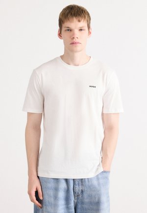 Hvit bomulls t-skjorte med korte ermer, med en liten svart "HUGO"-logo på brystet. Kombinert med lyseblå denimshorts.