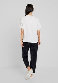 Biała krótka bluzka w kratkę z zapięciem na guziki z tyłu, zestawiona z czarnymi spodniami w białą kratkę i casualowymi butami.