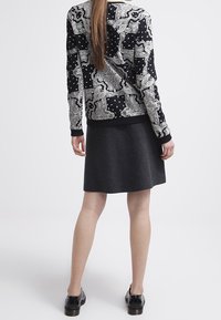 Svartvit mönstrad tröja med intrikata mönster, parat med en mörkgrå kjol. Texturerat tyg och enkla svarta skor.