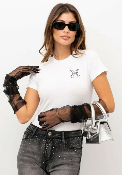 Guanti neri trasparenti con bordi arricciati, t-shirt bianca attillata con logo, jeans neri strappati con strass, borsa argentata, occhiali da sole neri.