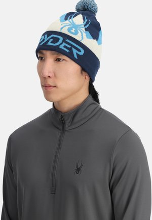 Berretto di maglia navy e crema con pom-pom, caratterizzato da una grafica di ragno sovradimensionata e testo "SPYDER" in azzurro chiaro. Texture morbida, design sportivo.