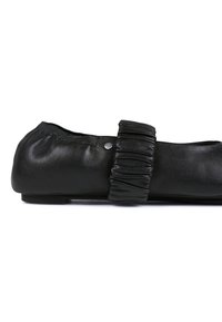 Zapato plano de cuero negro con detalle de tira recogida, textura suave y suela baja, con un pequeño acento metálico en el costado.