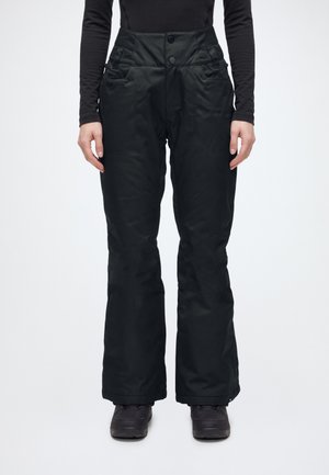 Le mannequin se tient face à l’avant, vêtu d’un pantalon de neige noir évasé à taille haute et à deux boutons, avec un haut noir et des bottes.