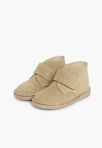 Béžové semišové kotníkové boots s plochým podpatkem a suchým zipem. Měkká textura s viditelným prošíváním podél podrážky pro zvýraznění detailu.