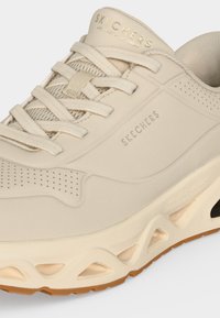 Близък план на бежова маратонка Skechers с връзки, перфорирани детайли и омекотена подметка с изрязани шарки.