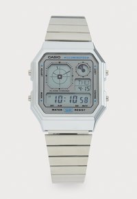 Montre Casio Illuminator avec un bracelet en métal argenté. Elle présente un boîtier rectangulaire blanc, un affichage numérique et des accents bleus pour les fonctions d'alarme et de mode.