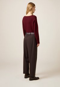 Bordowy sweter z dzianiny o luźnym kroju, zestawiony z ciemnymi spodniami z wysokim stanem i wzorzystym paskiem. Brązowe botki do kostek dopełniają całość.