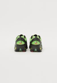 Black and neon green sneakers feature a textured mesh upper, cushioned heel, and a rubber sole with accent colors red and yellow.
