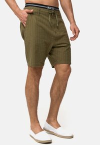 Olivenfarvede shorts lavet af tekstureret stof med lodrette striber, der har en drawstring talje og sidelommer. Båret med hvide slip-on sko.