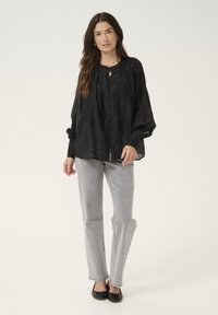 Camicia nera trasparente con scollatura rotonda, abbottonatura frontale e maniche a campana, abbinata a jeans grigi chiari a gamba dritta e ballerine nere.