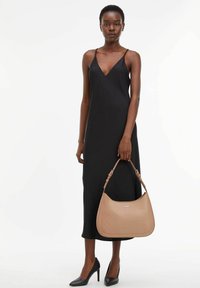 Robe noire à bretelles, sac à épaule beige avec logo en relief, chaussures noires à talons hauts, design minimaliste, texture de tissu lisse.