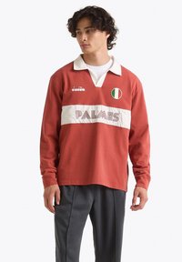 Maglia da rugby a maniche lunghe rossa con una striscia bianca, caratterizzata dal testo "PALMES", un emblema della bandiera italiana e un colletto bianco a contrasto.