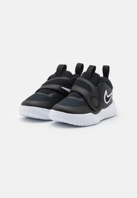 Zwarte sportieve schoenen met een bovenwerk van mesh, klittenbandsluiting en een witte rubberen zool. Beschikt over twee trekringen en een subtiele logo aan de zijkant.