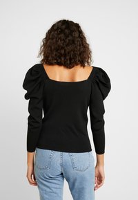 Zwart trui met opgeblazen mouwen, vierkante halslijn, aansluitende lijfje, zachte textuur en ribbelmateriaal. Draag het met lichtblauwe high-waisted jeans.