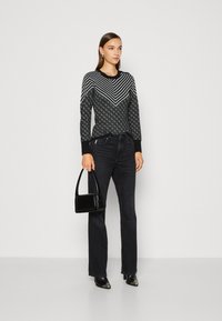 Černý svetr s dlouhými rukávy, zdobený vzory šípů a diamantů, spárovaný s černými džíny a malou lesklou kabelkou. Černé boty na podpatku doplňují celkový vzhled.