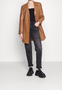 Blazer extragrande de estampado de serpiente marrón, top negro ajustado, jeans gris oscuro de corte tapered y zapatos negros de cordones gruesos. Textura suave, ajuste holgado.